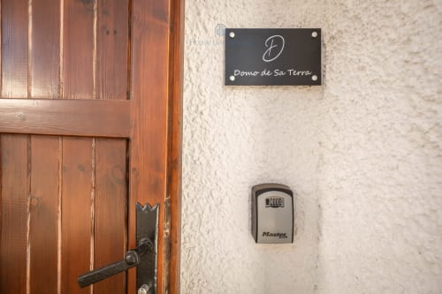 Wooden door with nameplate for Domo de Sa Terra villa in Quartu Sant'Elena, Master Lock keybox on beige wall
