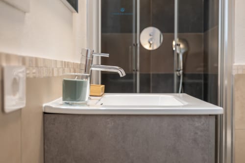 Lavabo moderno con rubinetto cromato presso House Live Express a Cagliari, con vanità scura e box doccia in vetro