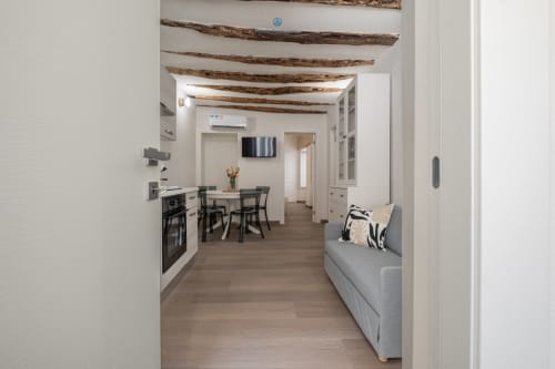 Cucina e zona living di un moderno appartamento con soffitto in legno a vista, divano grigio, tavolo da pranzo e angolo cottura a House Live