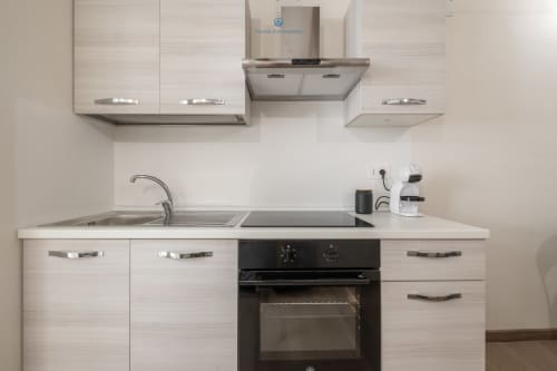 Cucina moderna nell'appartamento House Live Express con armadi bianchi, forno nero, piano cottura, lavello e cappa in acciaio inossidabile