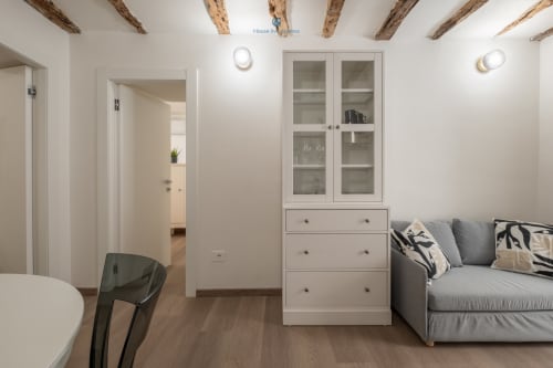 Zona living moderna con divano grigio, mobili bianchi, travi a vista e pavimenti in legno presso House Live Express