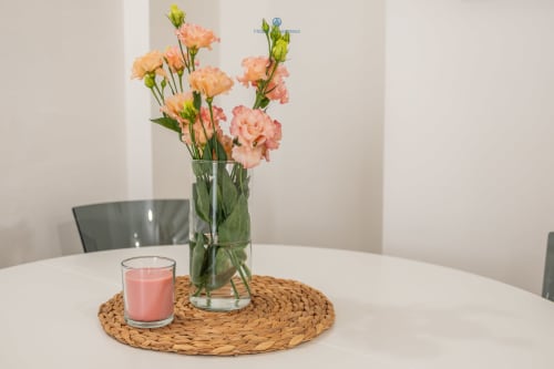 Garofani color pesca in vaso di vetro con candela rosa su sottopiatto tessuto nell'appartamento House Live Express a Cagliari