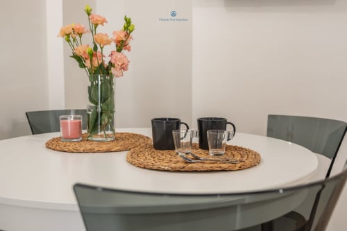 Tavolo da pranzo moderno a House Live Express Cagliari con garofani rosa, tazze nere e tovagliette intrecciate