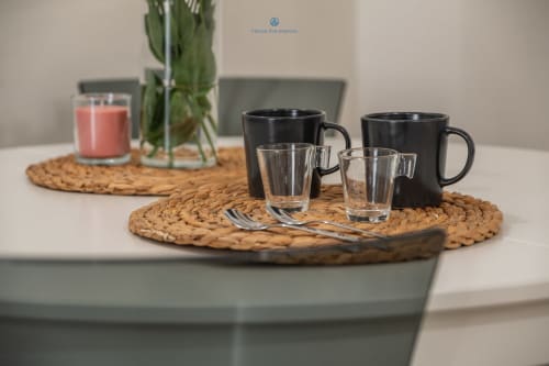 Tazze nere, bicchieri e candela su sottobicchieri intrecciati nell'appartamento House Live Express a Cagliari