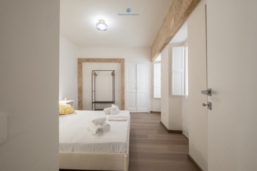 Camera spaziosa presso House Live Express a Cagliari con letto bianco, travi in legno e arredi moderni