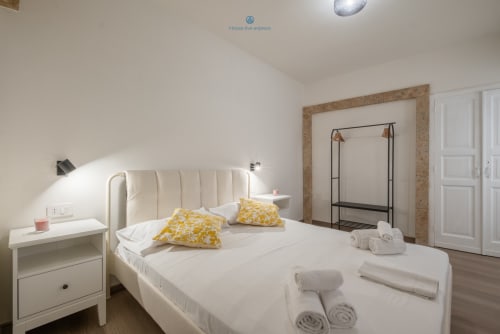 Camera moderna di House Live Express a Cagliari con letto color crema, cuscini gialli, arredi bianchi e vista sul giardino