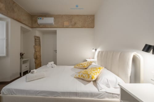 Camera moderna di House Live Express a Cagliari con letto bianco, cuscini gialli, aria condizionata e arredamento minimalista