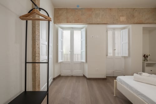 Camera luminosa e accogliente a House Live Express Cagliari, con letto, pareti in sughero, porte bianche, pavimenti in legno e attaccapanni