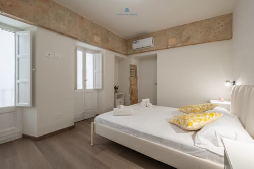 Camera moderna presso House Live Express a Cagliari con letto bianco, cuscini gialli, soffitto in sughero, aria condizionata e giardino