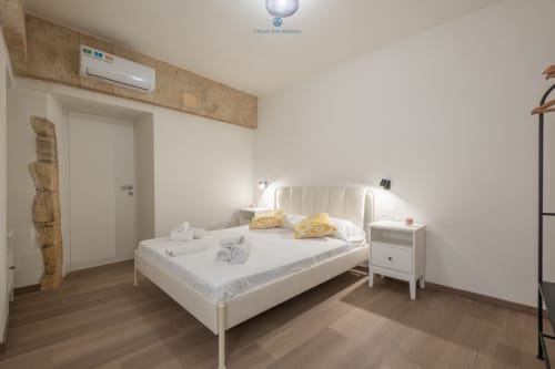 Camera moderna di House Live Express a Cagliari con letto queen, comodino bianco e aria condizionata