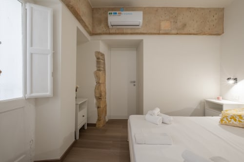 Camera da letto moderna presso House Live Express a Cagliari con letto bianco, aria condizionata, travi in legno e arredamento minimalista