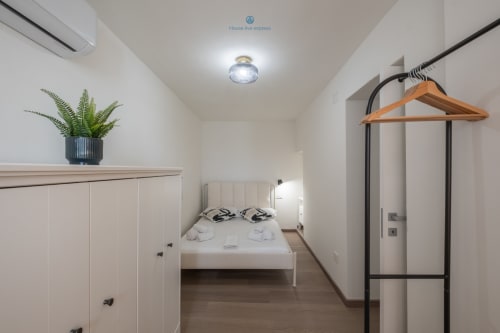 Camera moderna presso House Live Express a Cagliari con letto bianco, arredo minimalista, pianta in vaso e appendiabiti in legno