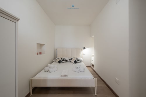 Camera da letto luminosa e minimalista con letto bianco, testata moderna e pavimento in legno, House Live Express Cagliari