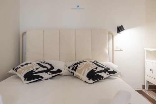 Luminosa camera da letto presso House Live Express Cagliari con testata imbottita color crema, biancheria bianca e cuscini a motivi neri