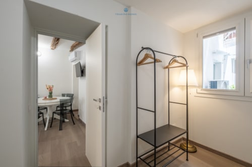 Camera da letto moderna presso House Live Express Cagliari con appendiabiti metallico, grucce in legno e zona pranzo visibile