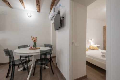 Zona pranzo moderna con tavolo rotondo bianco, sedie nere e vista sulla camera da letto presso House Live Express, Cagliari