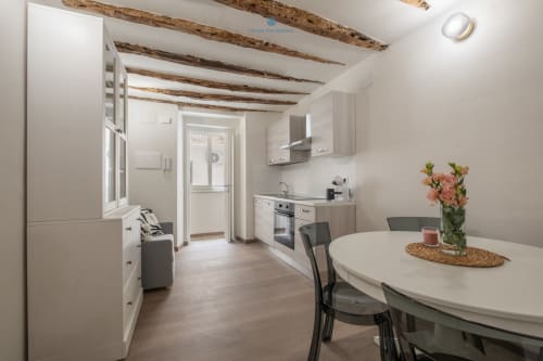 Moderna zona cucina-pranzo a House Live Express Cagliari con travi in legno a vista, mobili bianchi, tavolo da pranzo e giardino
