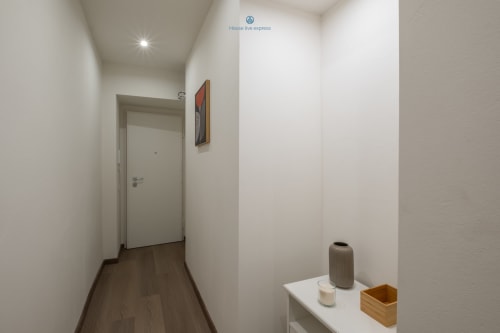 Corridoio luminoso e moderno dell'appartamento House Live Express a Cagliari, con pareti bianche, pavimento in legno e illuminazione incassata