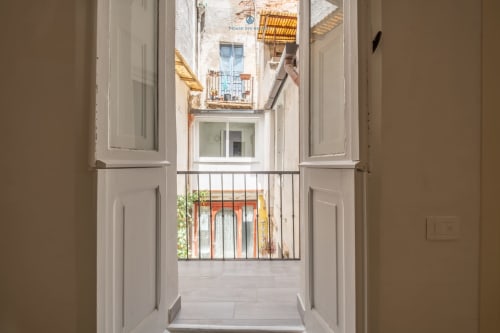 Porte-finestre aperte che rivelano la vista del balcone sulla città di Cagliari, appartamento House Live Express con tetti in cotto visibili