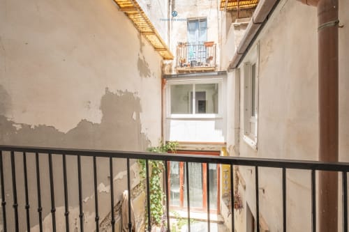 Stretto cortile della House Live Express a Cagliari con muri invecchiati, ringhiera nera, piante in vaso e finestre