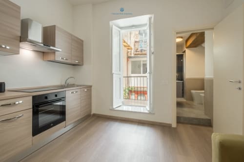 Cucina moderna con mobili in legno, fornello e porta che si affaccia sul balcone con vista sulla città presso House Live Express Cagliari