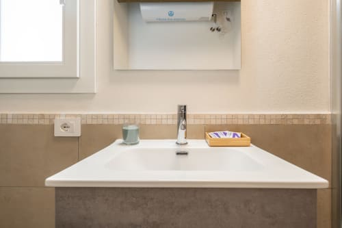 Lavabo moderno con bacino bianco, rubinetto cromato e rivestimento in piastrelle beige presso House Live Express Cagliari