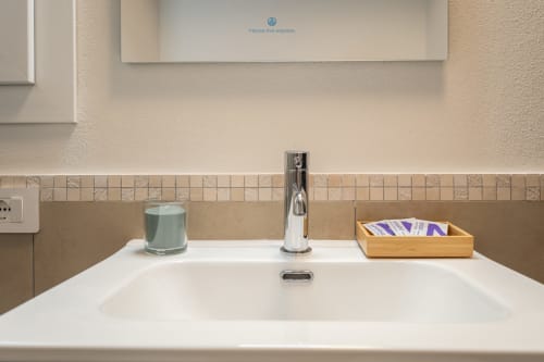Lavabo moderno con rubinetto cromato, candela menta e vassoio in legno nell'appartamento House Live Express a Cagliari