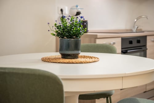 Cucina moderna nell'appartamento House Live Express con fiori blu in vaso su tavolo rotondo bianco, sedie verdi e acciaio inossidabile