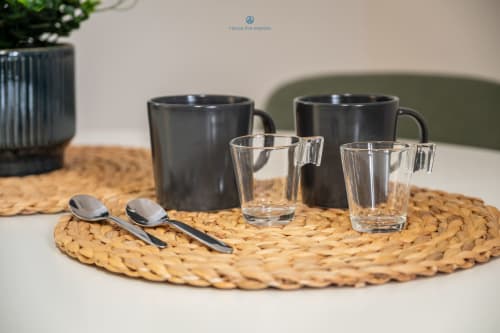 Tavola moderna con tazze, bicchieri e cucchiai su sottopiatto intrecciato presso House Live Express, Cagliari