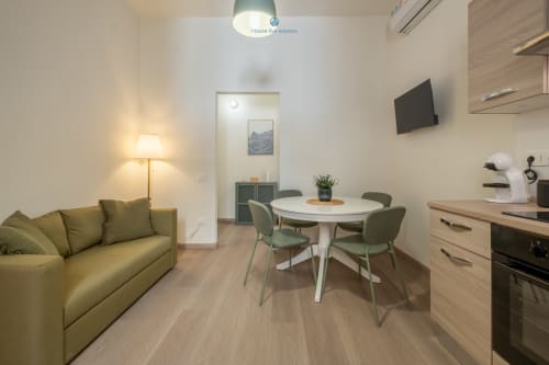 Zona living moderna con divano verde, tavolo da pranzo, cucina e TV a schermo piatto presso House Live Express a Cagliari