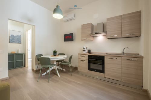 Cucina e zona pranzo moderna nell'appartamento House Live Express a Cagliari, con mobili in legno e sedie verdi