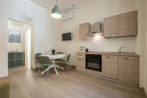 Zona cucina-pranzo moderna dell'appartamento House Live Express a Cagliari con mobili in legno, tavolo rotondo bianco e verde