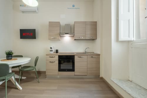 Cucina moderna e zona pranzo nell'appartamento di Cagliari con armadi in legno, fornello, tavolo da pranzo e Netflix sulla TV
