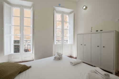 Camera da letto moderna e luminosa in House Live Express, Cagliari con armadi bianchi, porte-finestre, vista sulla città e servizi alberghieri