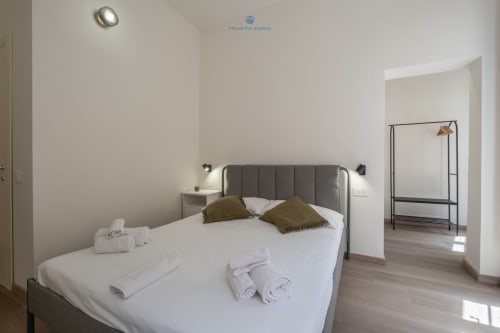 Camera da letto moderna presso House Live Express a Cagliari con letto rivestito grigio, biancheria bianca e pavimento in legno