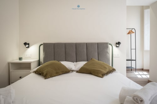 Camera da letto moderna in appartamento a Cagliari con testata imbottita grigia, biancheria bianca, cuscini oliva e arredamento minimalista