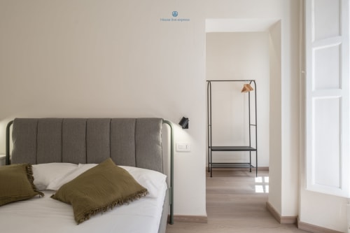Camera moderna a House Live Express, Cagliari con letto imbottito grigio, biancheria bianca, cuscini verdi e appendiabiti in metallo