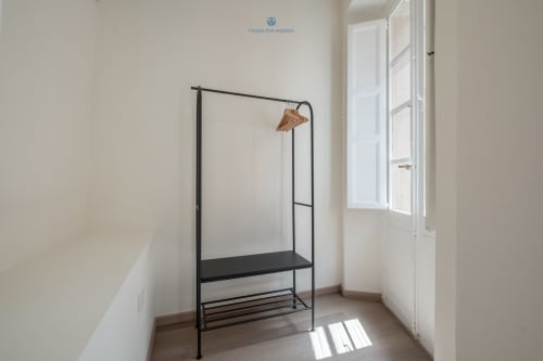 Camera minimalista presso House Live Express a Cagliari con appendiabiti in metallo nero e grucce in legno accanto alle porte bianche