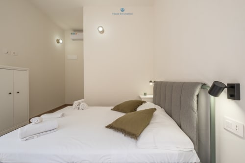 Camera moderna presso House Live Express a Cagliari con testata grigia, biancheria bianca, cuscini color oliva e climatizzatore