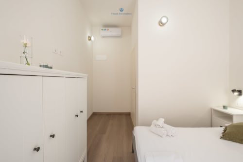 Camera da letto compatta con armadio bianco, pavimento in legno, letto con asciugamani, unità AC presso House Live Express Cagliari