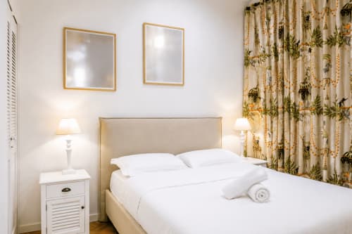 Elegant bedroom at Enjoy Nice hotel in Nice featuring a beige bed, golden-framed mirrors, botanical curtains, and white