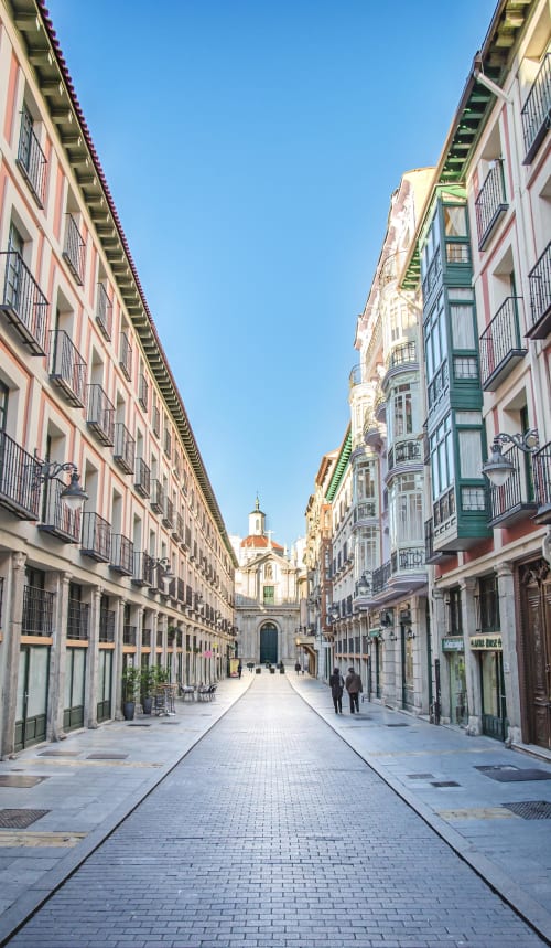 Calle peatonal en Valladolid conducente a iglesia con edificios históricos y cielo azul despejado