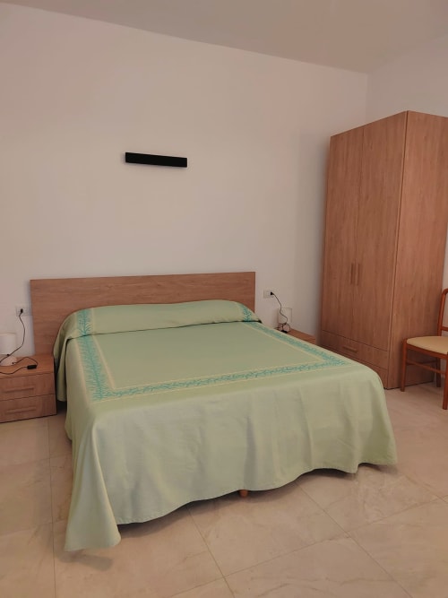 Camera spaziosa a La Locanda Guesthouse in Sardegna con letto in legno, copriletto color crema, armadio in legno e pavimento piastrellato