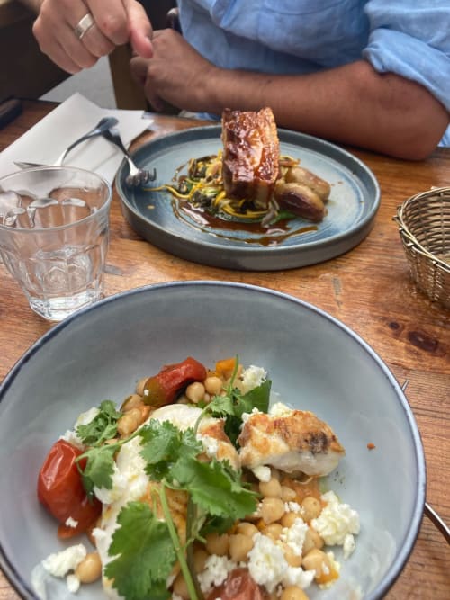 Fine dining at Agriturismo Colle Mura: plated dishes with roasted meat, chickpeas, fresh cheese, and herbs on wooden table