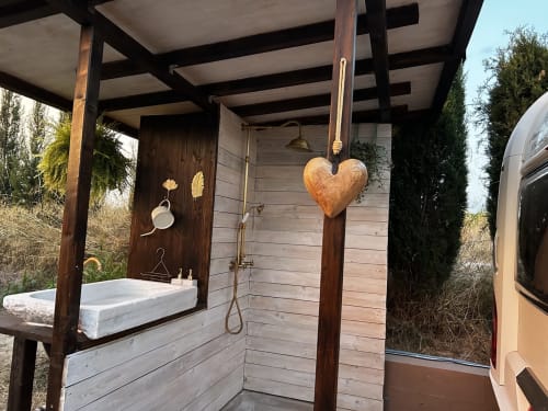 Outdoor shower at B&B Wine And Cooking Penedès with wooden pergola, white sink, hanging heart decoration, and cypress trees