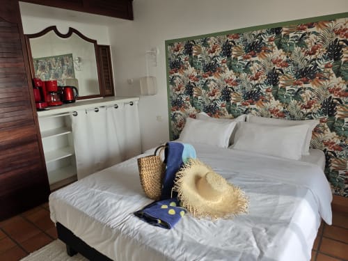 Chambre Suite Azur au Clémara Evasion avec tête de lit tropicale fleurie, draps blancs, chapeau de paille et vue sur la mer en Martinique