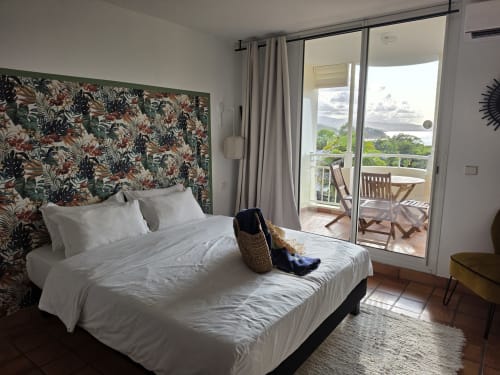 Chambre Bright Suite Azur à Clémara Evasion avec tête de lit fleurie, balcon vue mer et terrasse en Martinique