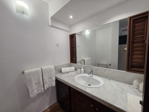 Salle de bains moderne avec vasque en marbre, lavabo blanc circulaire, grand miroir et portes en bois de la Suite Azur à Clémara Evasion
