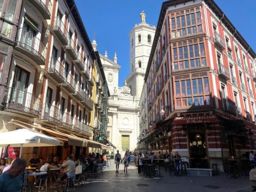 Calle histórica de Valladolid con edificios coloridos, terrazas de café e iglesia de fondo cerca del hotel Palacio Mambrilla