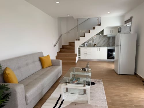 Ampla sala de estar integrada na vila Sunshine 85 House em Ribeira Brava com sofá cinzento, cozinha e escada de madeira